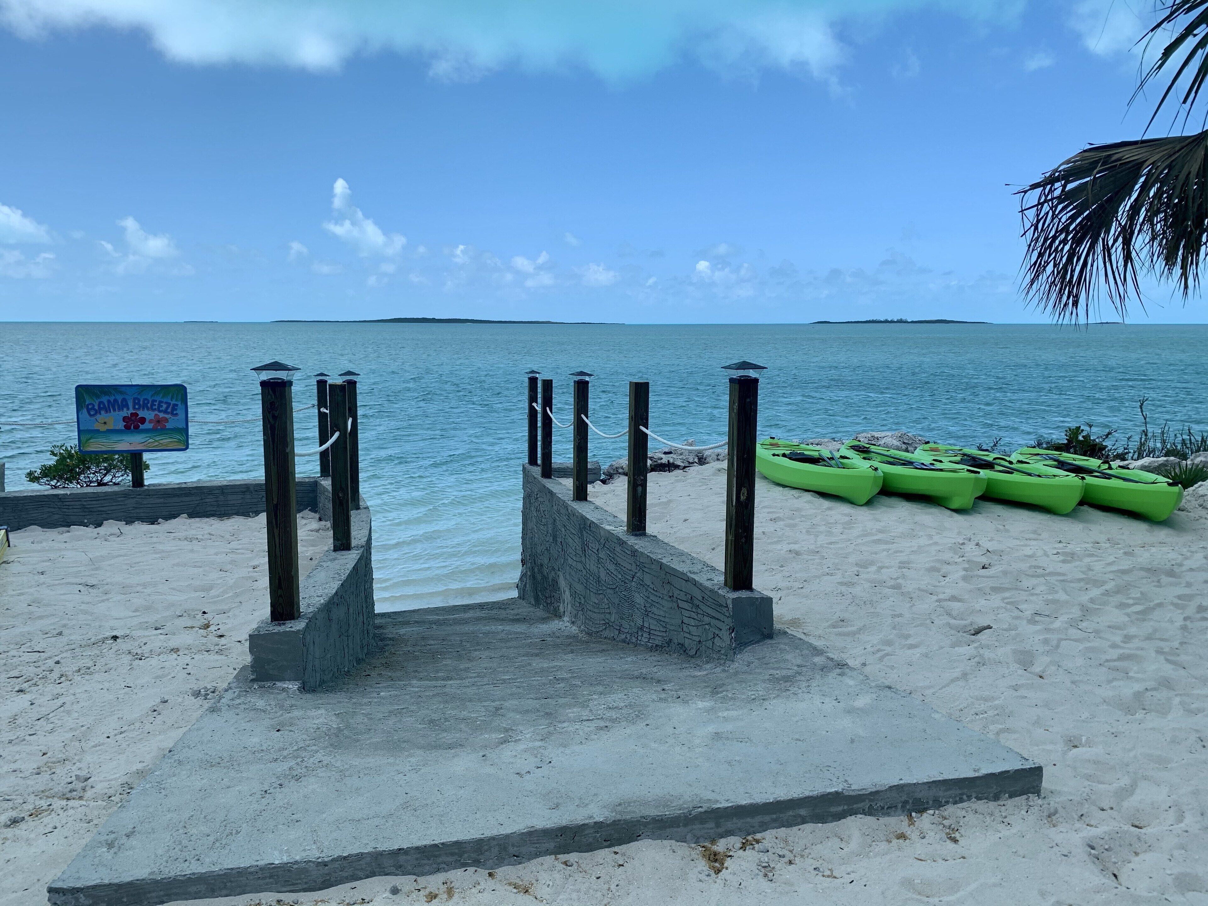A beach with a sign reading "Bama Breeze" and green kayaks lined up on the sand.