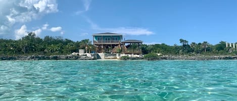 A beachfront property with a large house, clear turquoise water, and lush greenery.