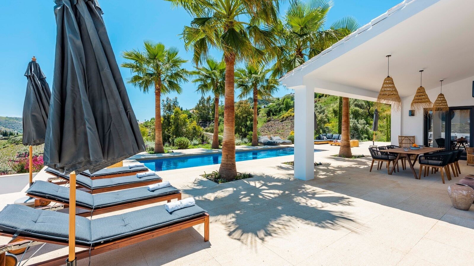 A poolside area with lounge chairs, a dining table, and umbrellas.