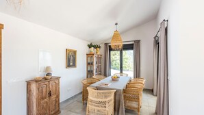 Een eetgedeelte met een tafel, stoelen, een houten kast, een hanglamp en een raam met gordijnen.