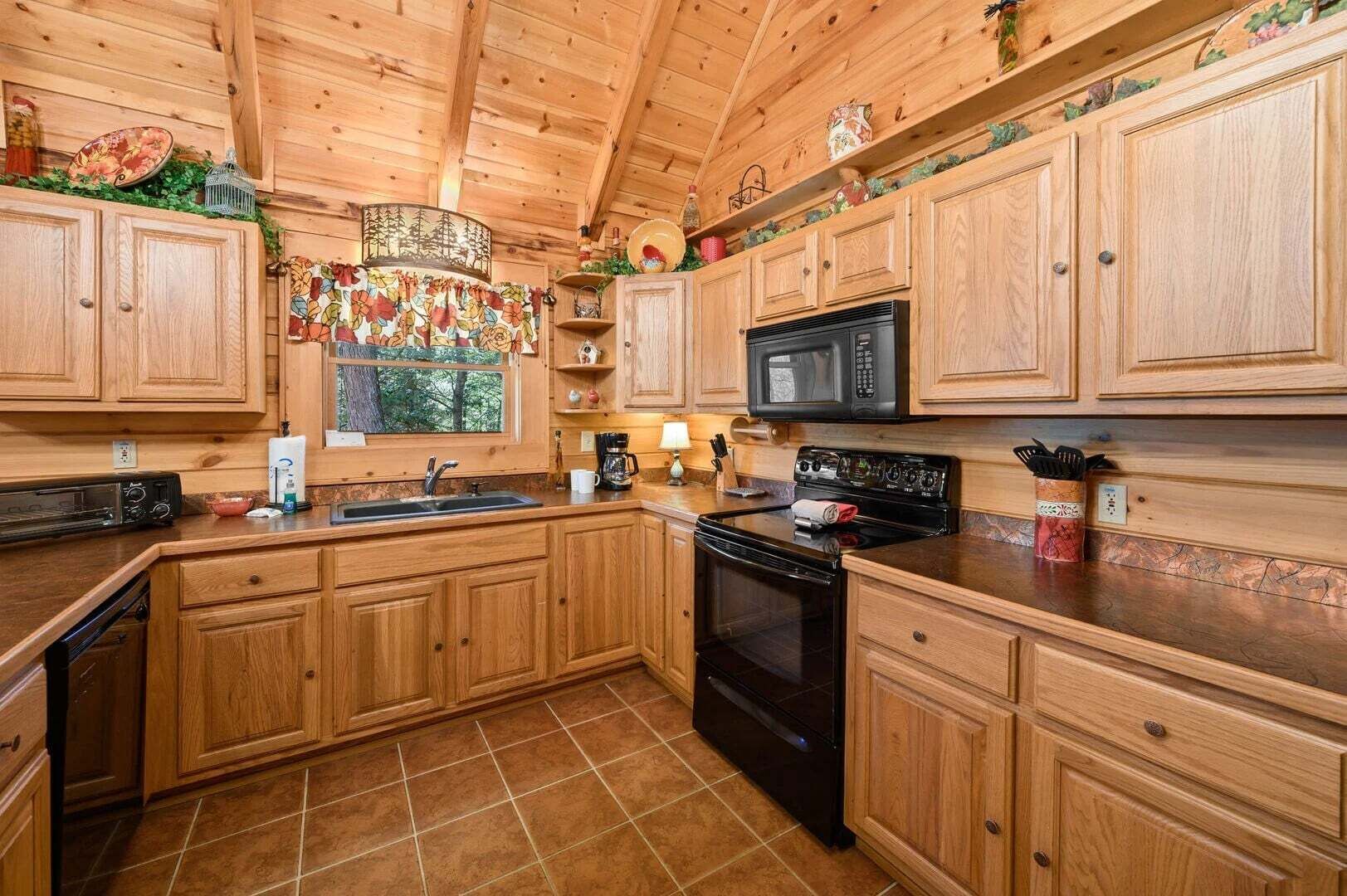 A wooden cabin kitchen with a stove, microwave, sink, and cabinets.