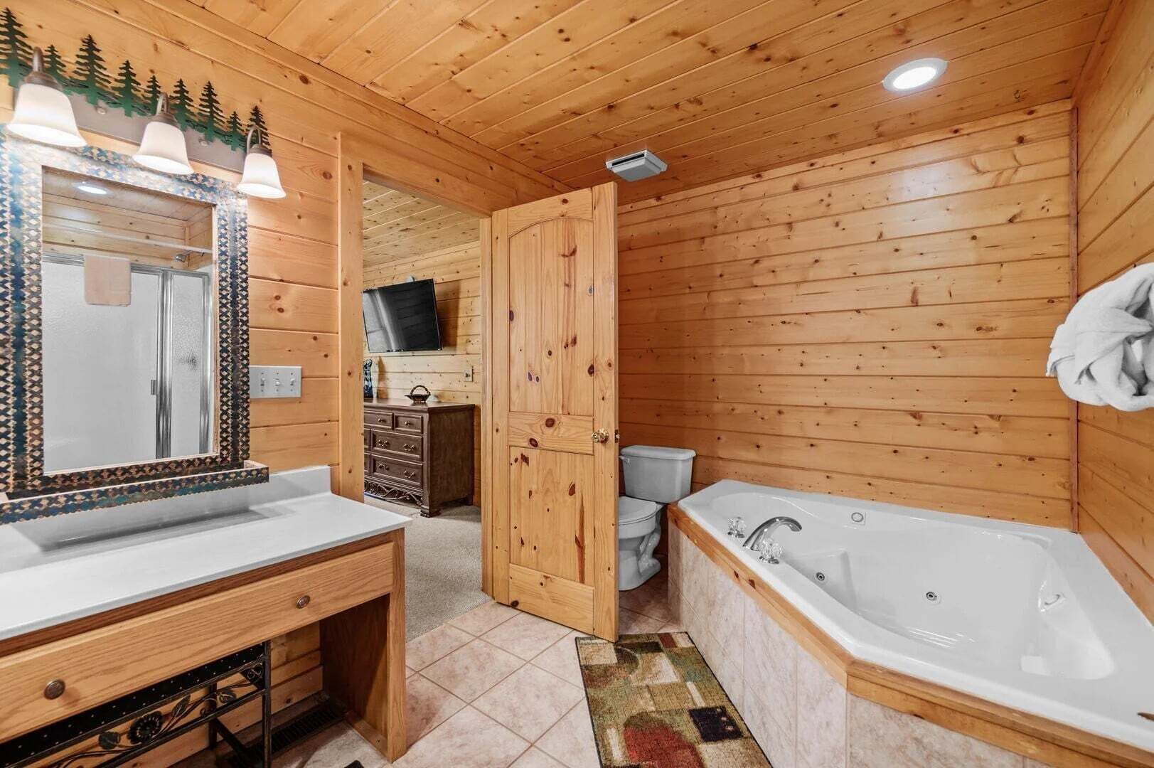 Een houten badkamer in een vakantiehuisje, met een wastafel, spiegel, wastafelmeubel, toilet en bad.