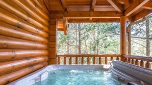 Una cabaña de madera con jacuzzi y vista al bosque.