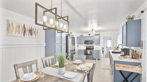 Una cocina moderna con armarios azules, una isla central y un comedor con mesas y sillas de madera.