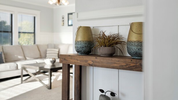 Una sala de estar con una mesa de centro de madera, un sofá y una estantería decorativa con jarrones y una planta.