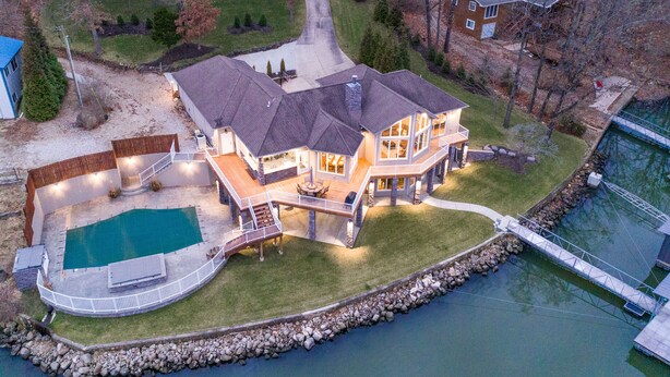 Una casa grande con piscina, un muelle y un muro de piedra alrededor del agua.