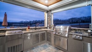 Una cocina al aire libre con detalles de piedra, una parrilla empotrada y vistas del paisaje circundante.
