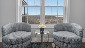 A room with two patterned armchairs, a small round table with a vase of flowers, and a large window offering a view of a hilly landscape. - Lovely Mountain Views Gatlinburg atop ChaletVillage HotTub GameRm Pets Sleeps10 (Gatlinburg)