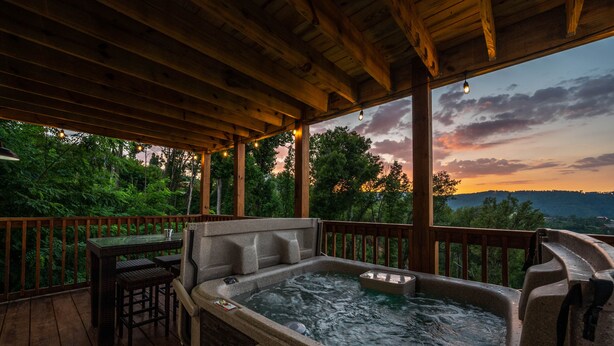 A hot tub on a wooden deck with a table and chairs, overlooking a forested area. - Lovely Mountain Views Gatlinburg atop ChaletVillage HotTub GameRm Pets Sleeps10 (Gatlinburg)