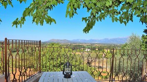 A balcony with a table and a lantern, overlooking a vineyard and mountains.