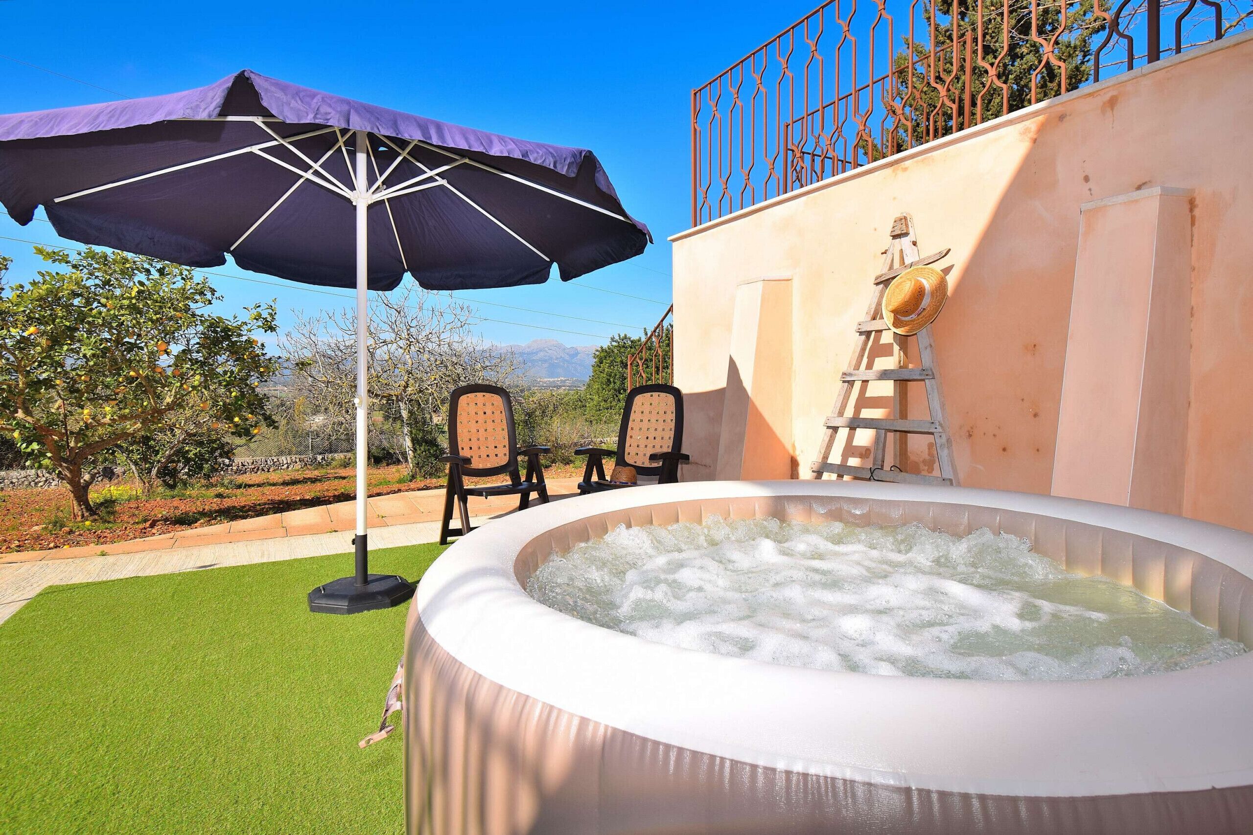 An outdoor hot tub with a ladder, two chairs, and a purple umbrella.