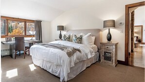 A bedroom with a large bed, a desk, and a chair. There is a window with a view of trees and a door leading to another room. - 4BR ski-in/out Beaver Creek condo with mountain views (Avon)