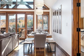 Un comedor con una mesa de madera, sillas y vistas a árboles otoñales a través de amplios ventanales.
