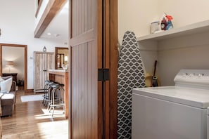Un área de lavandería con lavadora, cortina de ducha estampada y productos de limpieza en un estante.