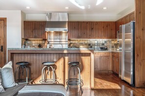 A modern kitchen with wooden cabinets, a stainless steel refrigerator, and a bar area with stools. - Charlie Rentz: Bachelor Gulch Ski-In/Out, Sleeps 12, Ritz Pool + Hot Tub Access, 2 King Suites (Avon)