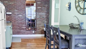 A dining area with a brick wall, wooden flooring, and a large wall clock.