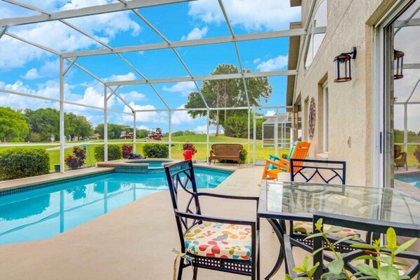 A covered outdoor swimming pool area with a glass table and chairs, surrounded by a white fence.