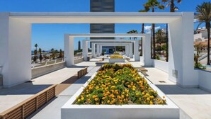 A modern architectural structure with a central garden of yellow and orange flowers, white walls, and a clear view of the sea. - Estepona Roof Top View by Interhome (Estepona)
