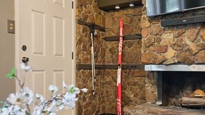 A stone fireplace with a flat-screen TV above it, a door with a keyhole, and skis leaning against the wall. - Completely Remodeled-- 1/1 just 2 blocks from the base! (Angel Fire)