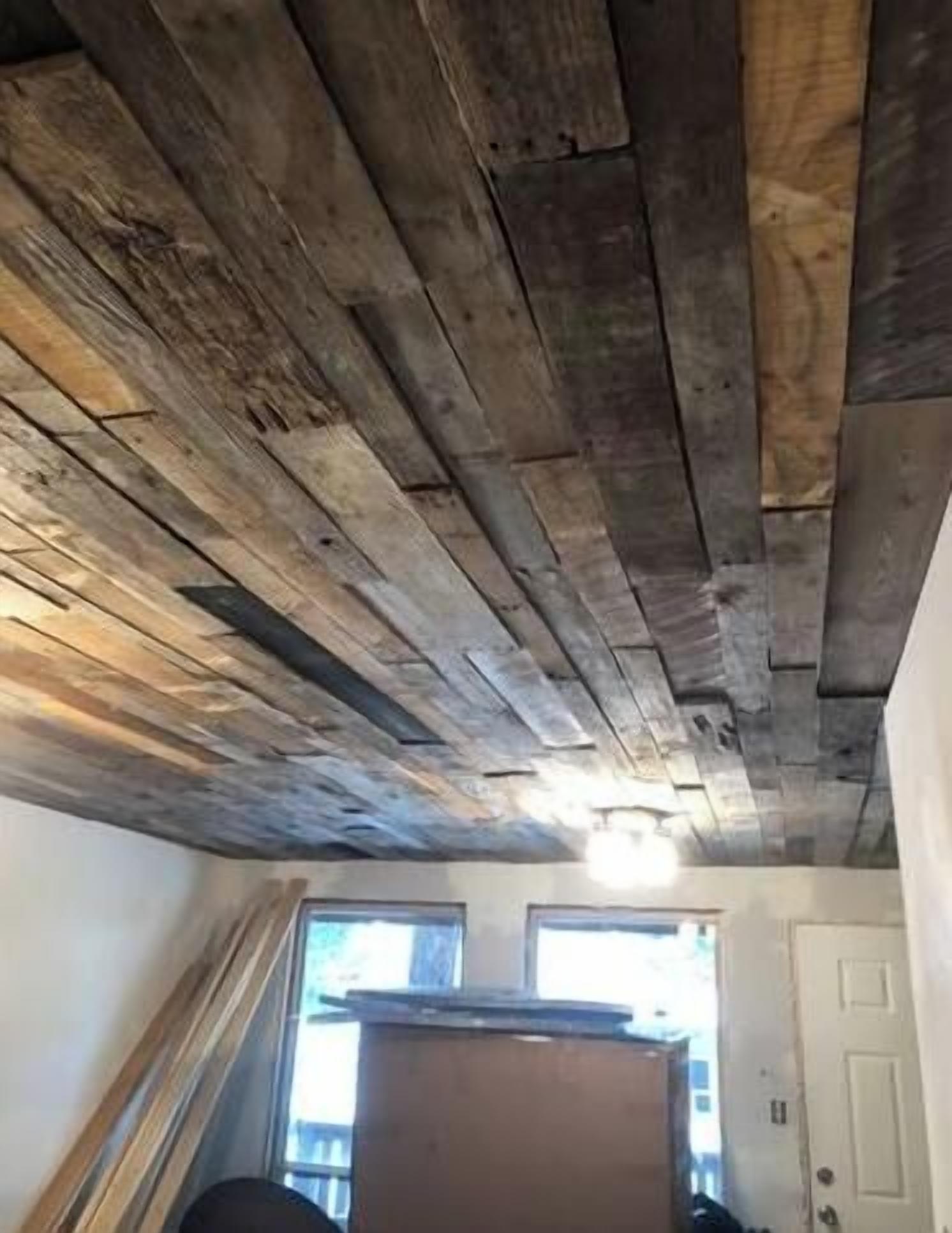A room with a sloped ceiling made of wooden planks, a window, and a door.