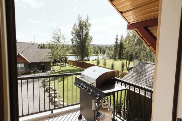 A balcony with a barbecue grill, a water heater, and a view of a residential area with houses and a lake.