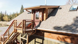 Una construcción de madera con techo inclinado, una escalera que lleva a una terraza y una chimenea.