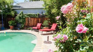 A backyard with a swimming pool, red lounge chairs, and blooming pink roses. - Modern poolside house with AC Downtown Mountain View! (Mountain View)