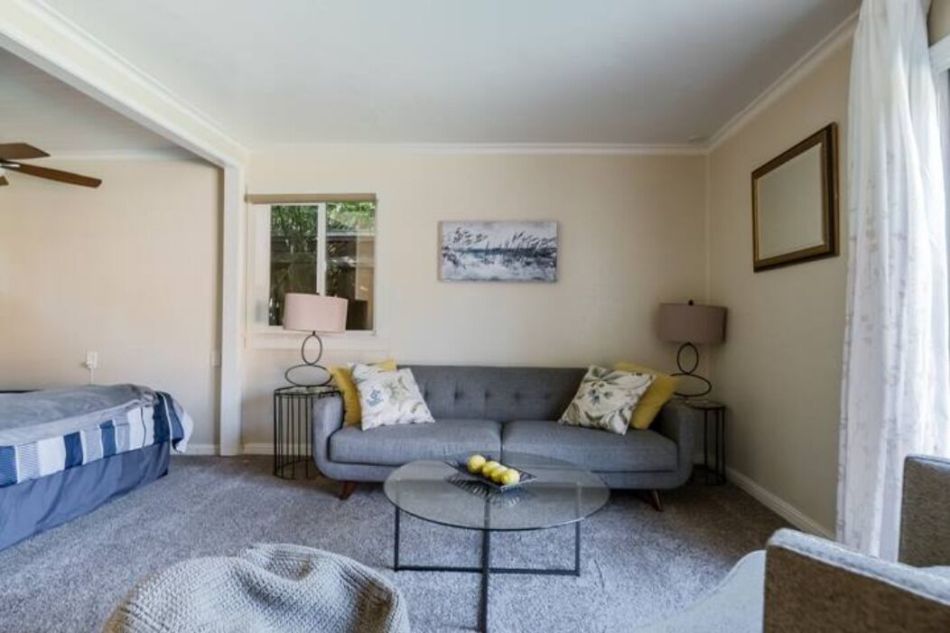 A living room with a grey sofa, a round coffee table, and a bed with a striped blanket.