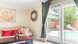 A living room with a sofa, a coffee table, a painting, a mirror, and a view of a backyard with a pool. - Modern poolside house with AC Downtown Mountain View! (Mountain View)