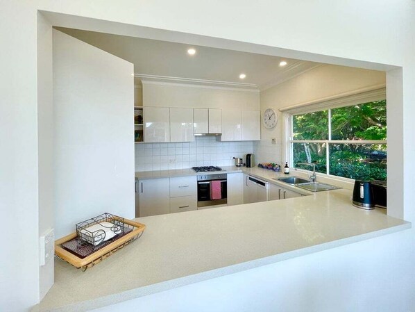 A modern kitchen with white cabinetry, a built-in stove, and a window with a view of greenery.