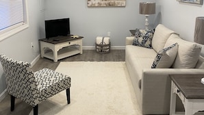 Una sala de estar con ventilador de techo, televisor, sofá, sillón estampado y alfombra.