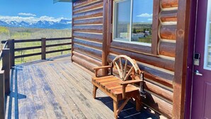 Uma cabana de tronco com um alpendre de madeira, um banco e vista para montanhas.