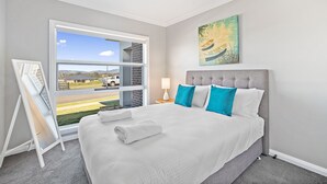 A modern bedroom with a large bed, a view through a sliding door, and a painting on the wall.