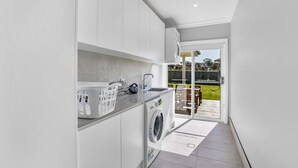 A modern kitchen with white cabinets, a washing machine, and a large window leading to a patio.