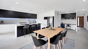 A modern kitchen with a central island, black bar stools, and a dining table with black chairs.