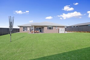 A residential house with a well-maintained lawn, a patio with outdoor furniture, and a large air conditioning unit. - Devan House - Your Innkeeper Mudgee (Mudgee)