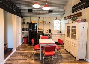 A compact kitchen with a refrigerator, stove, and dining area with red chairs.