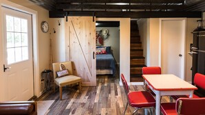 Una stanza accogliente con pavimento in legno, un divano, un tavolo da pranzo con sedie rosse e una scala che conduce a un'altra stanza.
