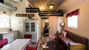 Un interno rustico con zona pranzo, divano, armadio e una porta con scritto “WELCOME TO THE RANCH”.