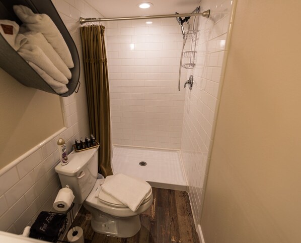 A small bathroom with a toilet, a shower, and a towel rack. - The Ranch Motel. Large cottage in a country setting with pool and hot tub. (Round Top)