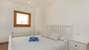 Una camera da letto con un letto, un comodino, un mobiletto, una finestra e un termosifone.