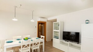 Una stanza moderna e luminosa con un tavolo da pranzo per quattro persone, una TV a schermo piatto e una parete attrezzata.