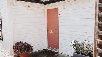 A white building with a red door marked with the number 2, a potted plant, and a doormat.