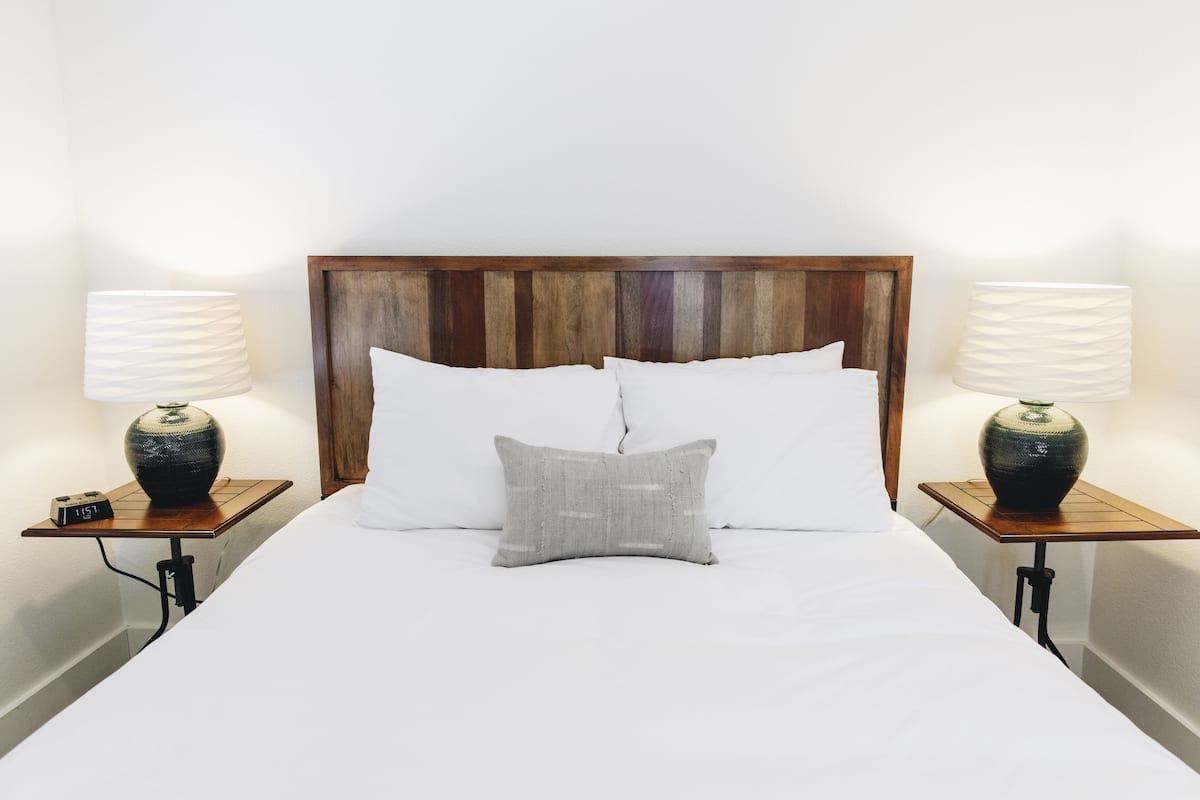 A neatly made bed with white linens, a wooden headboard, and two bedside tables with lamps and a clock.