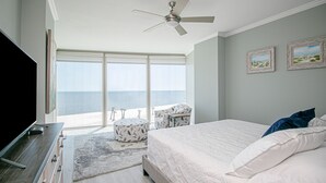 Ein Schlafzimmer mit einem großen Bett, einem Deckenventilator, einem Fernseher und Meerblick durch große Fenster.