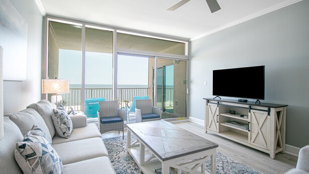Ein Wohnzimmer mit Sofa, Couchtisch, TV-Schrank und einem Balkon mit Sitzgelegenheiten.