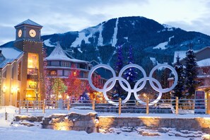 A hotel with a clock tower, Olympic rings, and snow-covered mountains in the background. - Modern Mountain Getaway (Whistler)