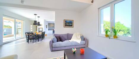 A spacious living area with a sofa, a coffee table, and a view of greenery through a large window.