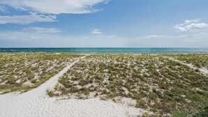 Una playa con arena, vegetación escasa, cielo despejado y mar tranquilo.