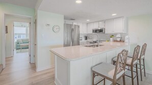 Una cocina moderna con armarios blancos, una isla central con taburetes y electrodomésticos de acero inoxidable, además de un reloj visible.